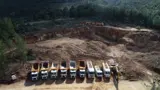 Fila di camion nella cava di bauxite ai piedi di una collina boscosa